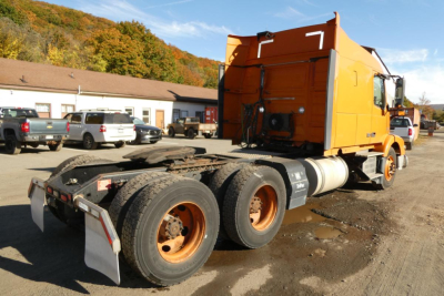 Semi truck chassis and cab of a 2016 Volvo VNM with orange paint, rear view showing dual rear axles and fifth wheel, identification visible on side.