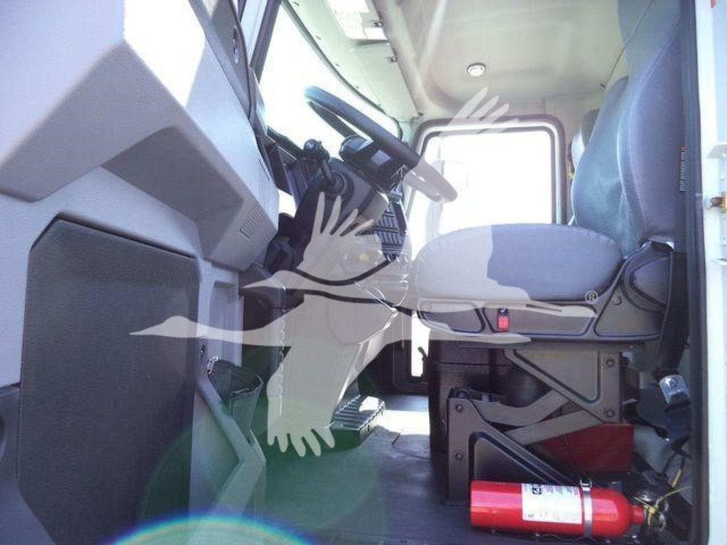Cab interior of a Mack MD6 truck showing driver's seat and steering wheel from side angle with dashboard and pedals.