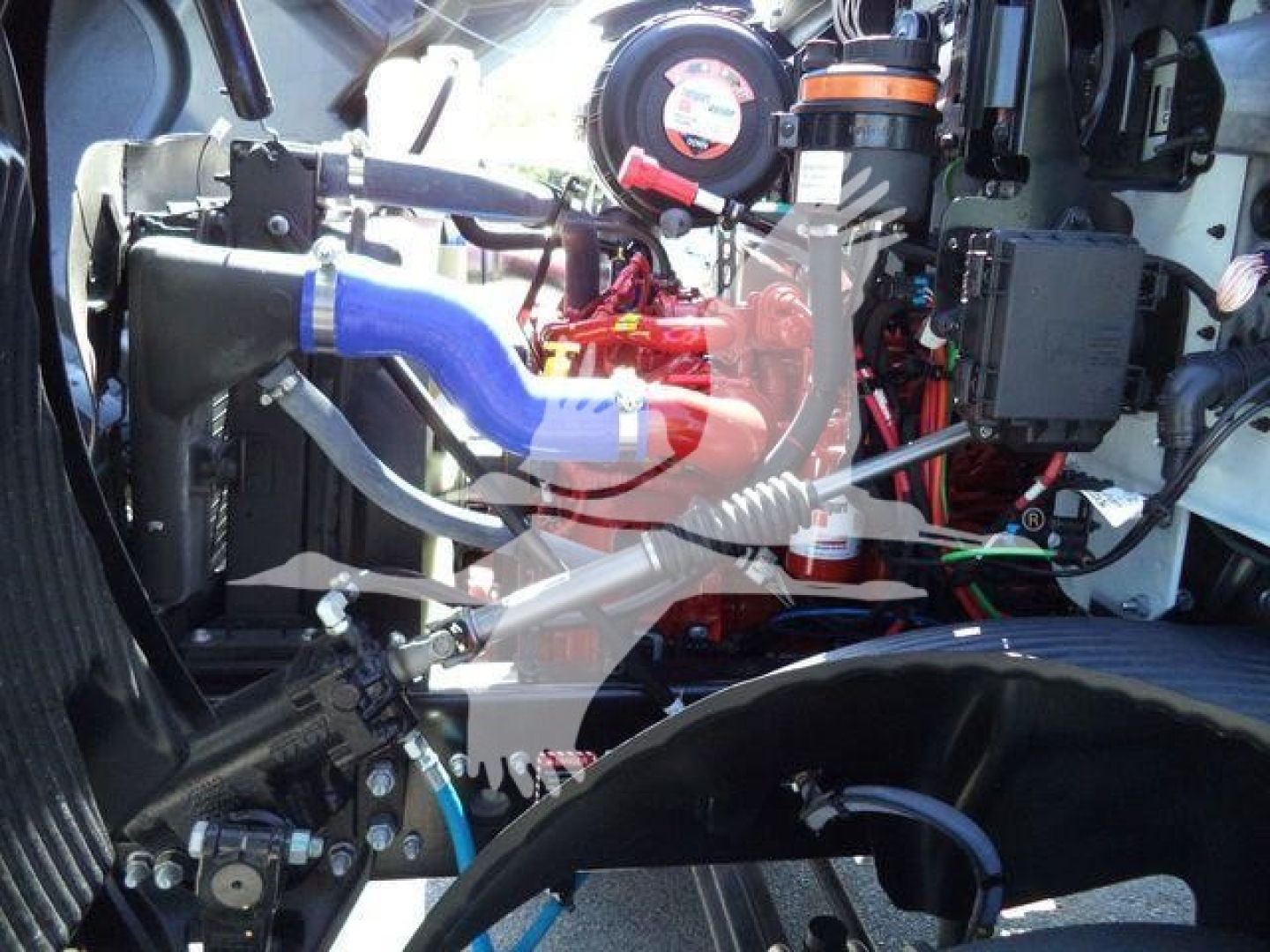 Mack MD6 engine bay showing blue and silver hoses, red engine components, orange clamps, wiring harness, and air intake tubing.