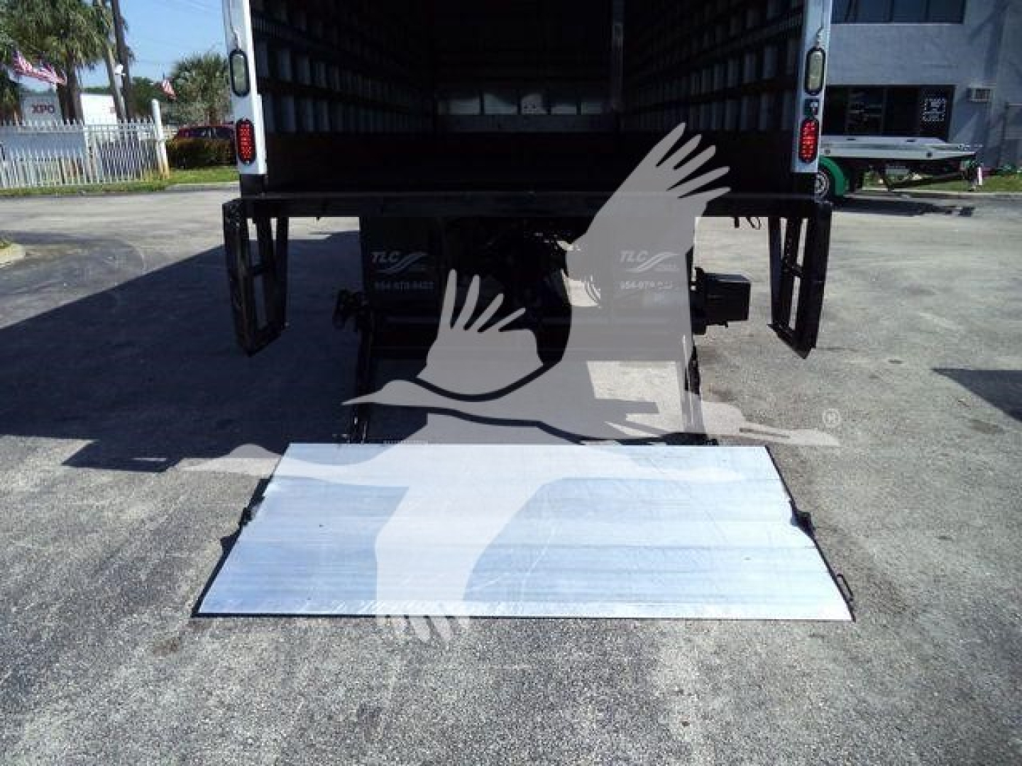 Truck tail with a lowered aluminum loading ramp extending from the back of a Mack MD6 box truck.