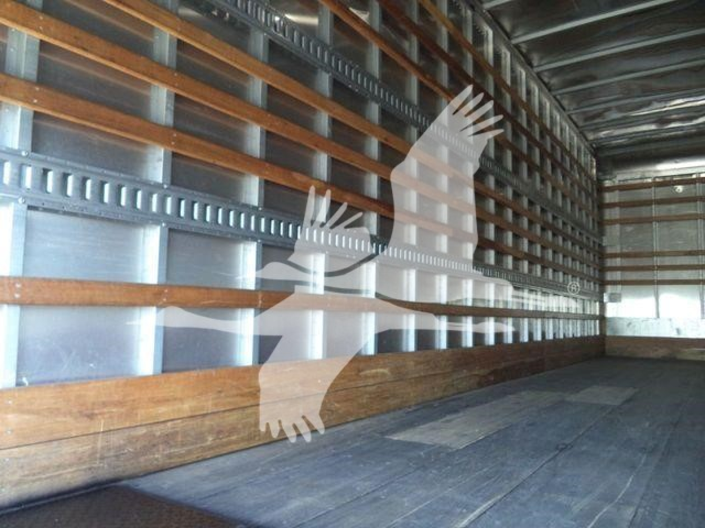 Trailer interior with metal side walls and wooden floor beam, empty cargo area showing structural ribs.