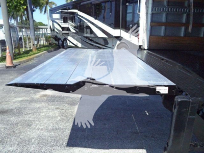 Flatbed truck bed on a new 2026 Mack MD6 in a lot, with a lifted aluminum platform and a shadow of a person.