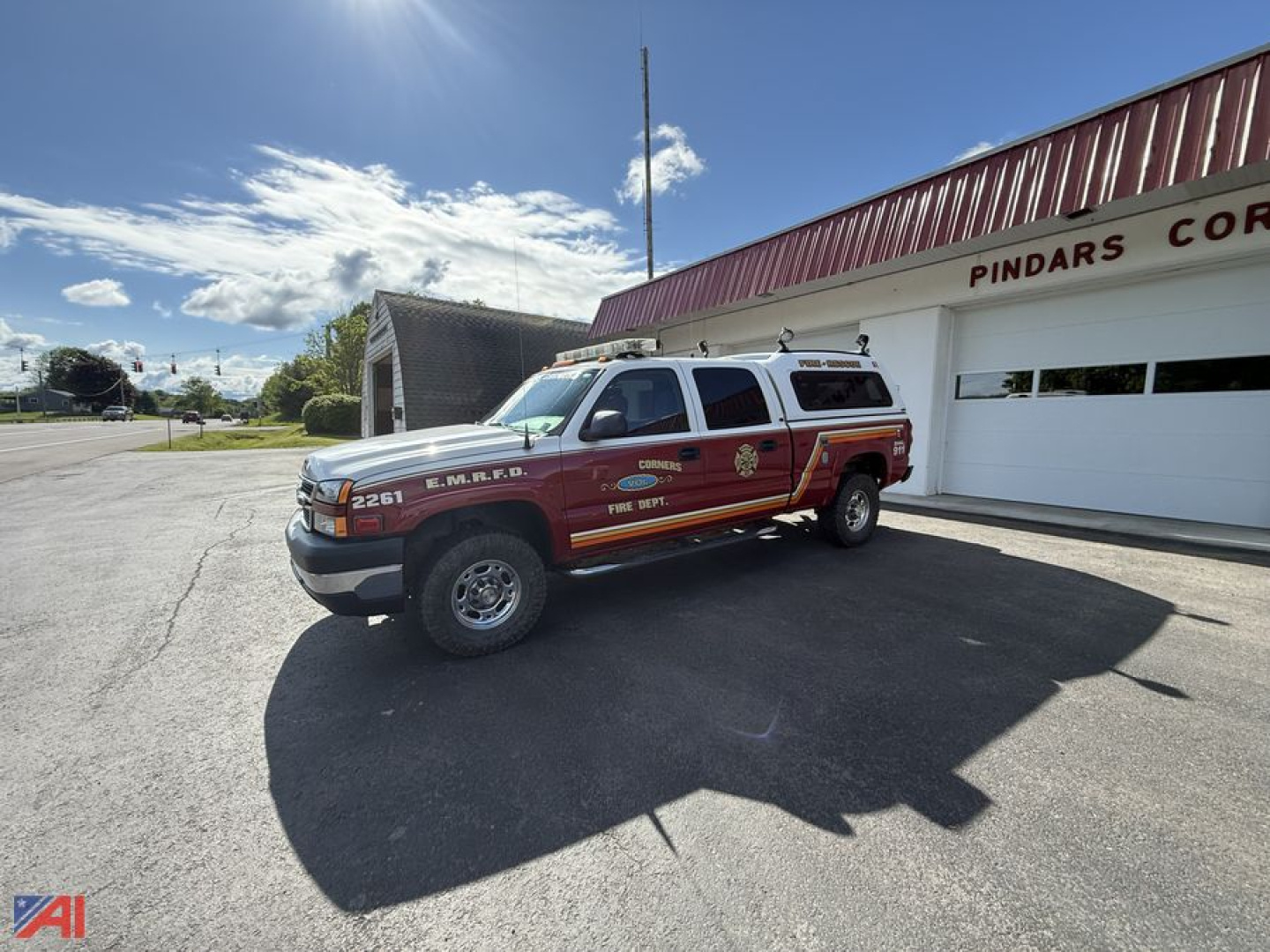 Chevrolet 2500HD emergency pickup truck with cap parked in front of a fire station-style building; red and gold emergency markings on the side.