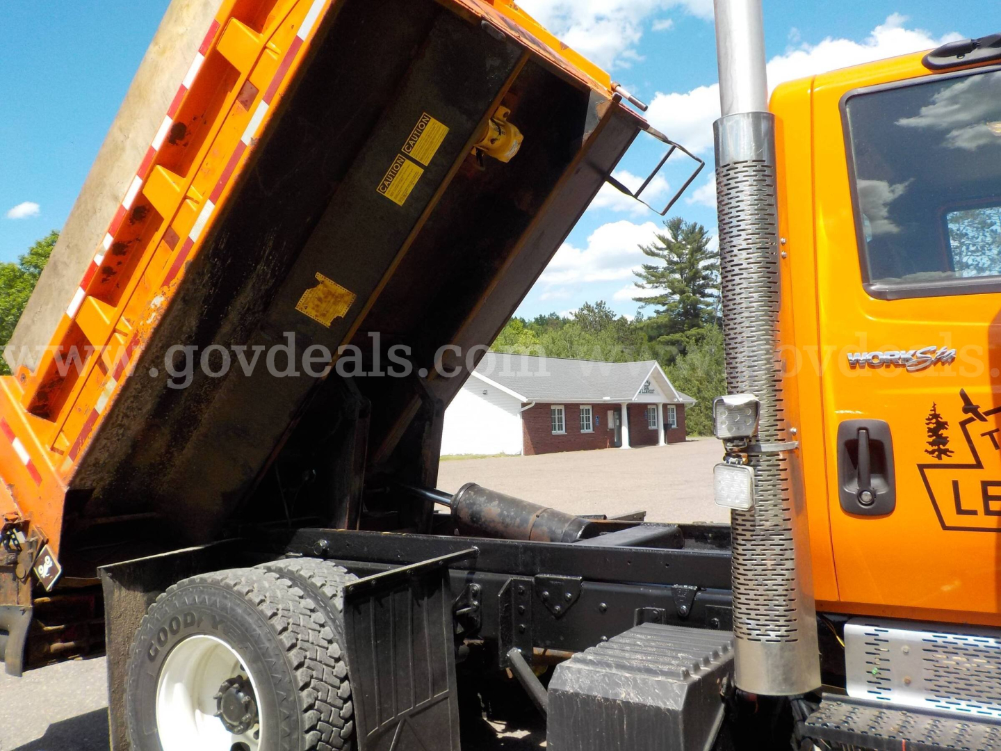Truck cab and raised dump body of an International 7400 plow truck showing orange cab and hydraulic lift.