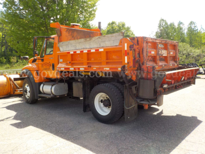 International 7400 plow truck in service with orange cab and plow equipment, side view showing fuel tanks and rear utility bed.