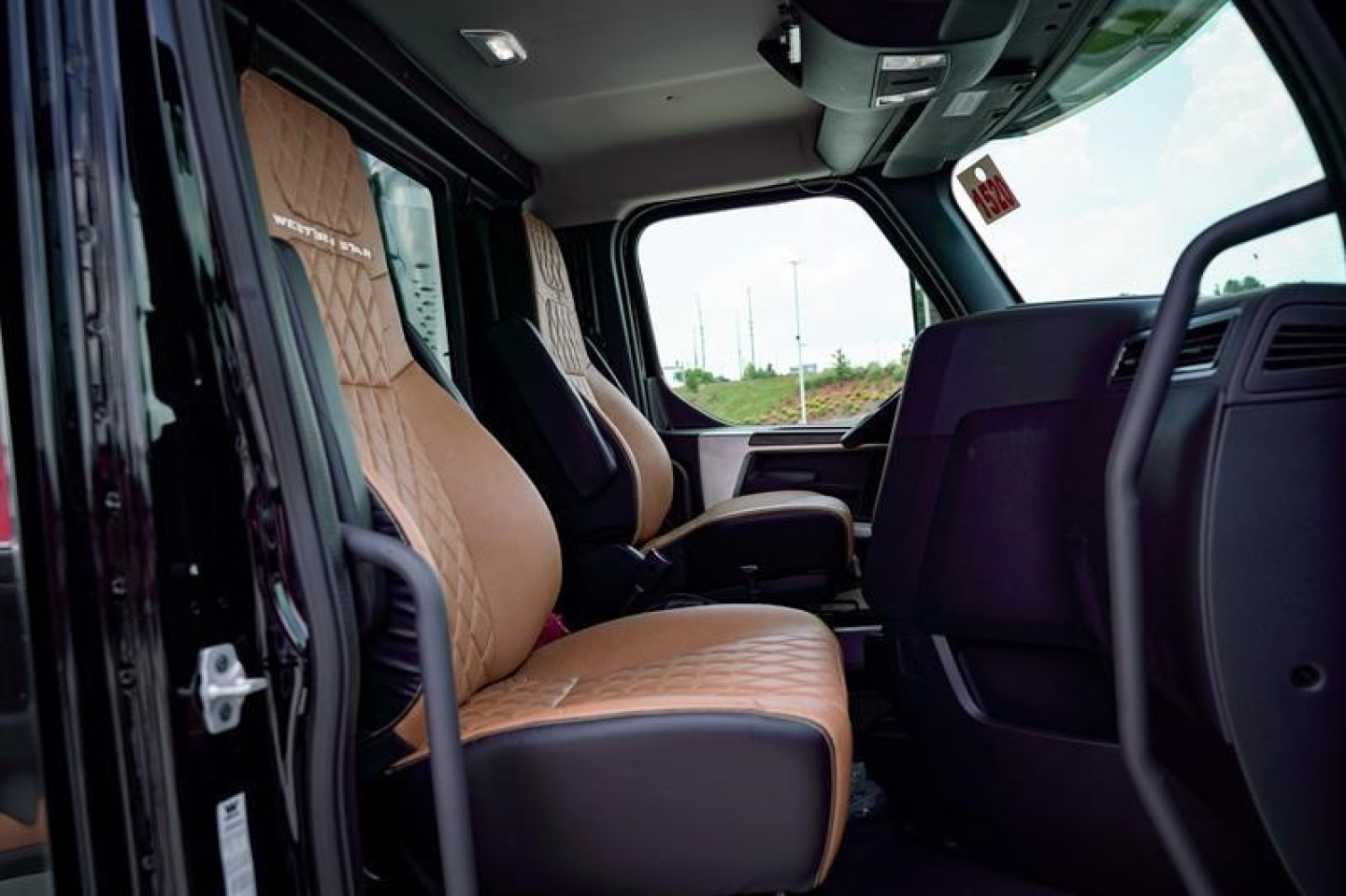 Truck cab interior showing tan leather seats and dark dashboard; open door view of Western Star 47X cab and driver seat area.