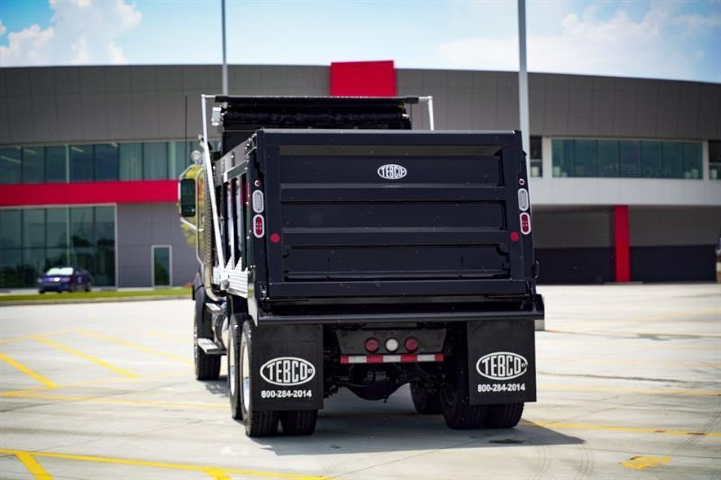 Dump truck rear view showing TBCB with dva mud flaps and rear lights in a parking lot.
