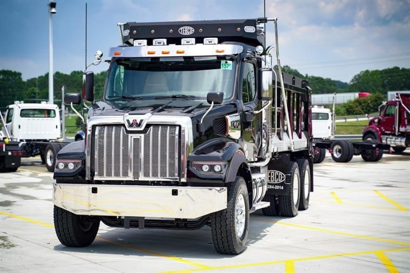 Western Star 47X dumping truck in a dealership lot showing front grille, chrome bumper, and dump bed with signage and lights.