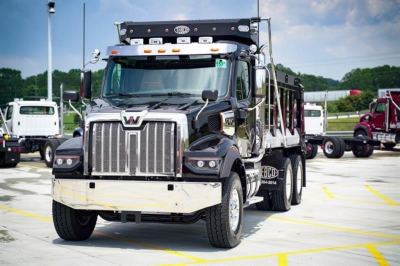 Western Star 47X dumping truck in a dealership lot showing front grille, chrome bumper, and dump bed with signage and lights.