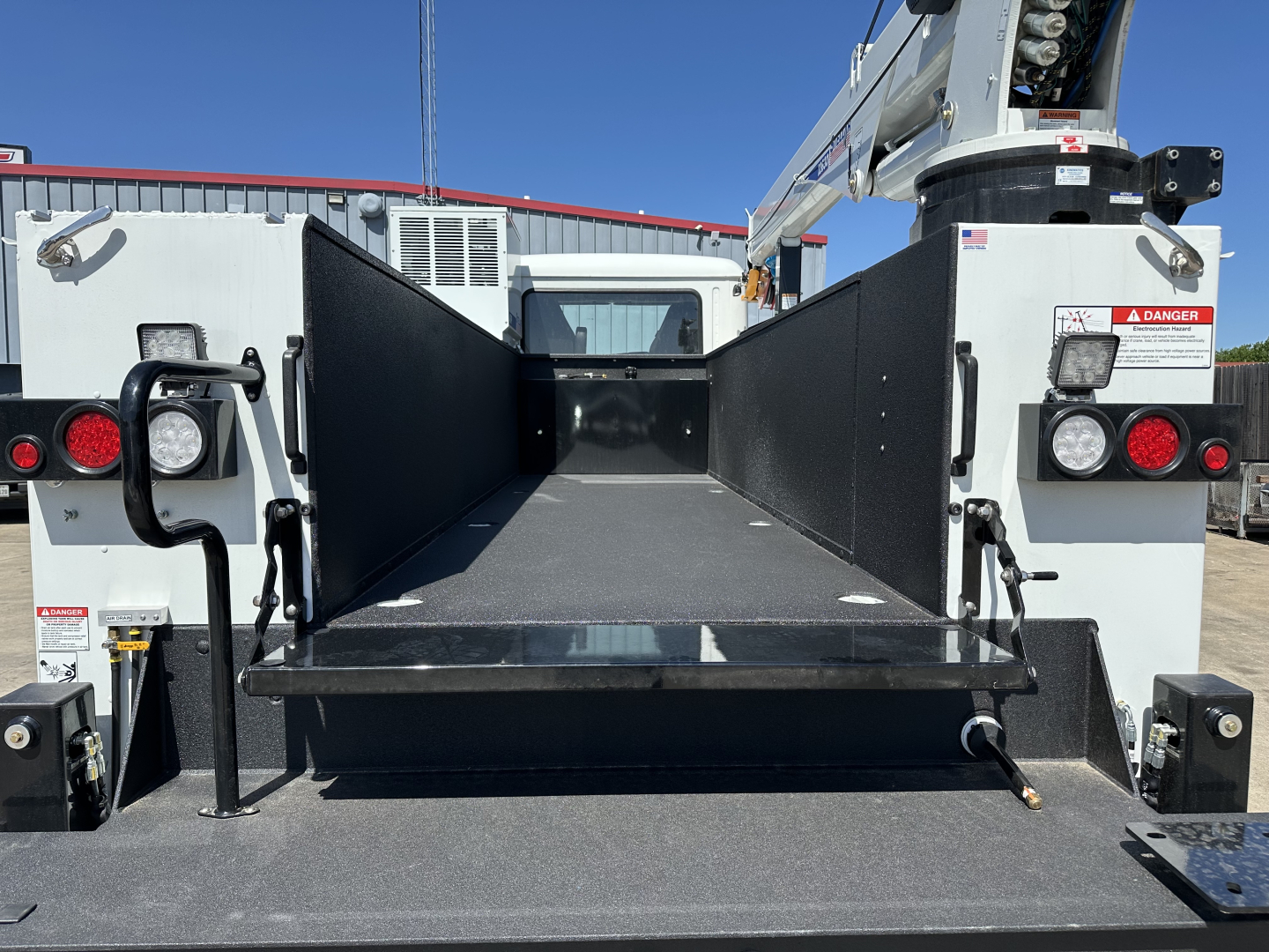 Truck bed or service body area of a 2026 Mack MD7, flatbed with side panels raised, showing empty cargo space and rear hydrualic mechanism.