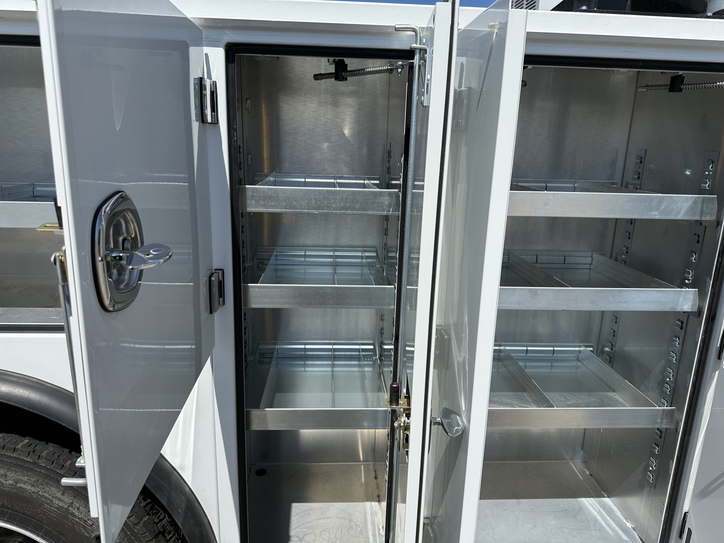 Service/Utility truck storage compartments open showing multiple empty aluminum shelves and secure locking mechanisms.