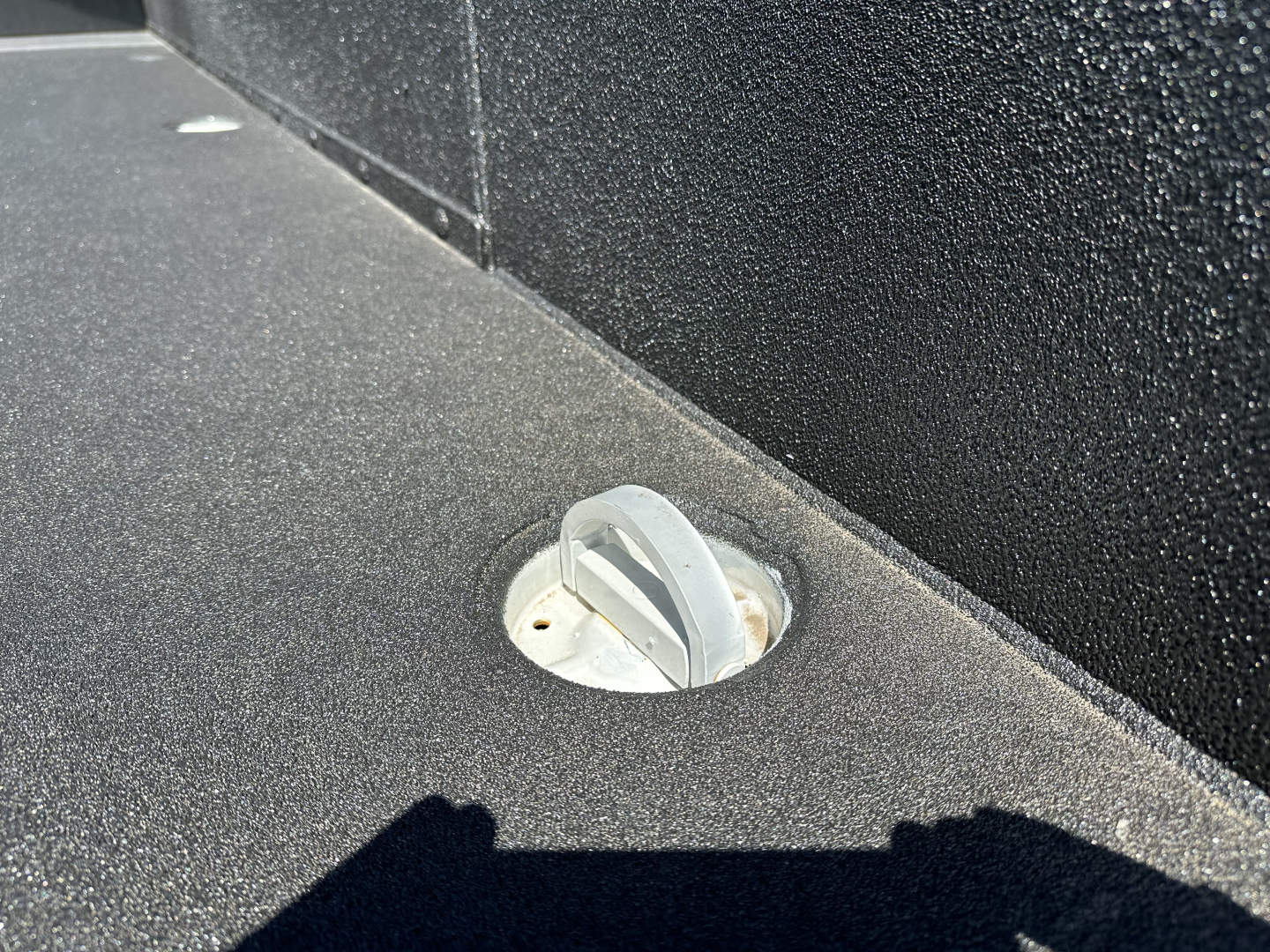 On a Mack MD7 truck bed deck, view of a circular recessed fuel or access cap with a gray twist-lock handle, surrounded by black textured surface.