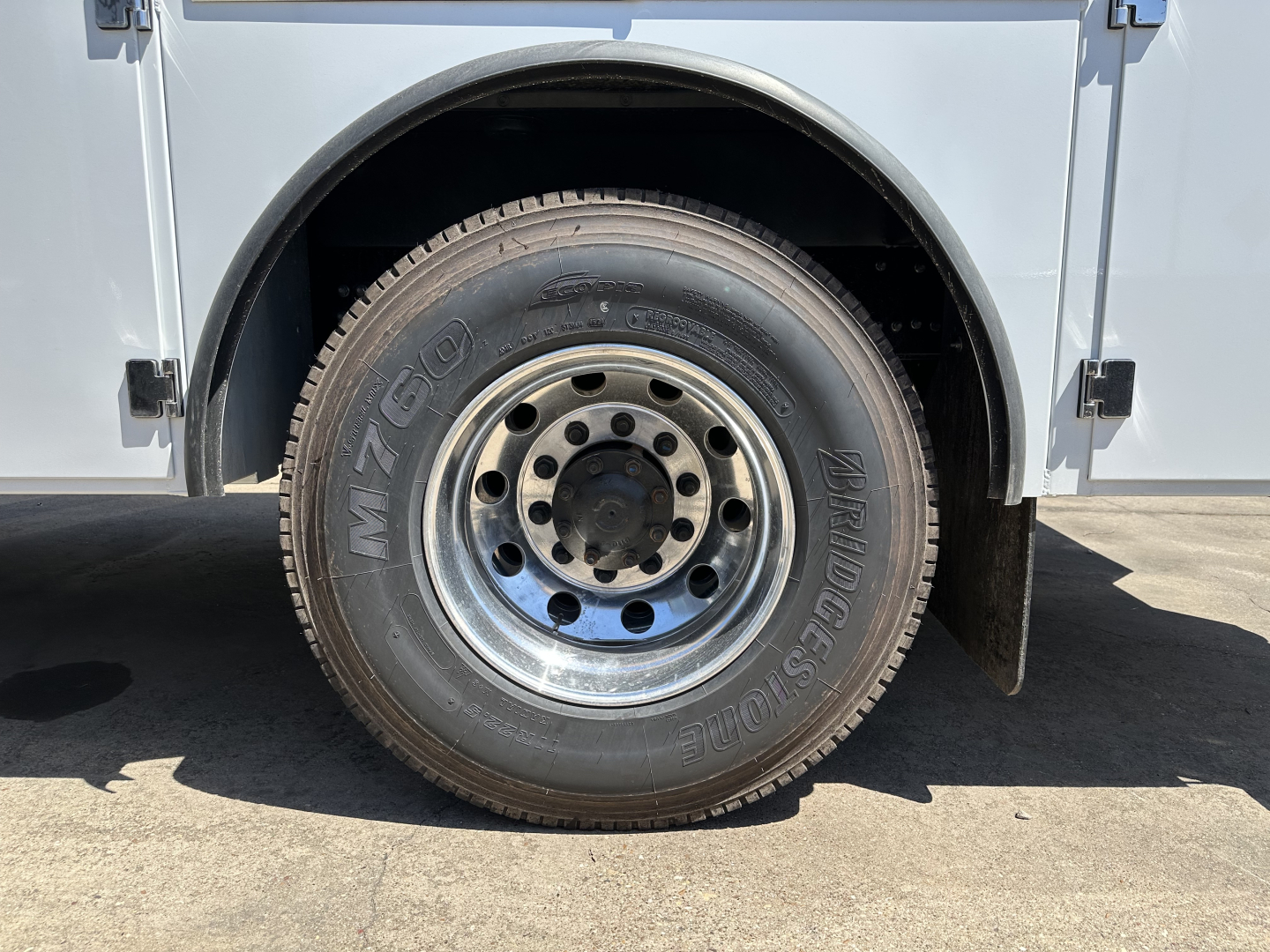 Front wheel of a service/utility truck showing M/S tire on steel wheel and fender with light gray body panel.