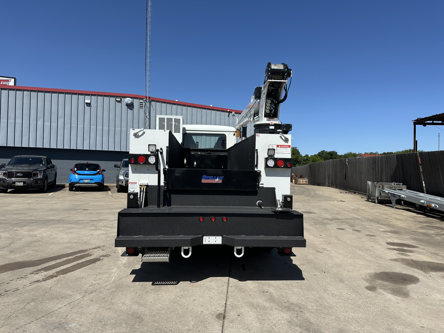 Rear view of a 2026 Mack MD7 service/utility truck with a hydraulic crane and flatbed; visible text includes BUILT BY MACK on the cab area, and general truck components.