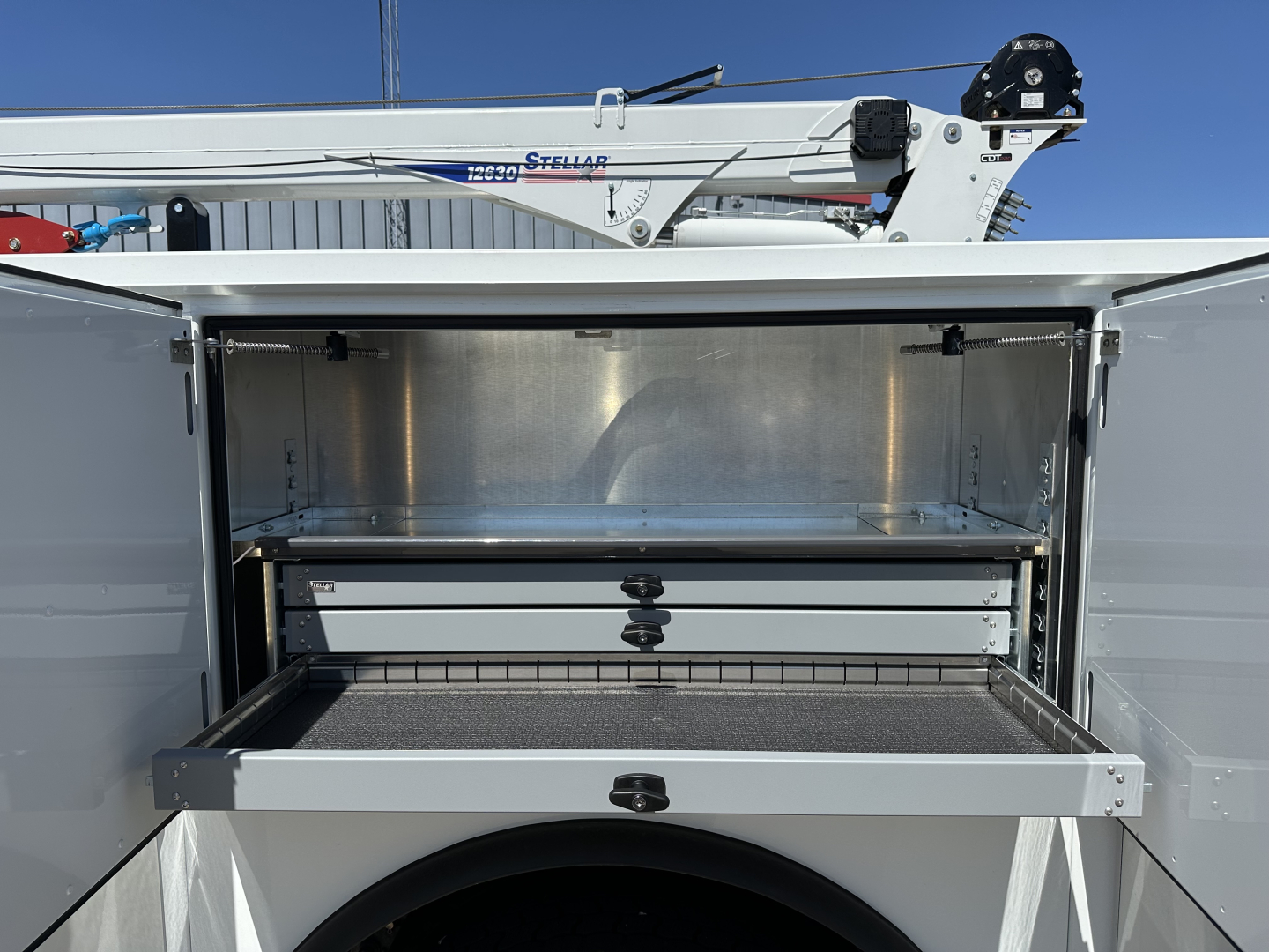 Truck service body with open storage compartments and a drawer, showing metal interior and a sliding tray in the lower bay.