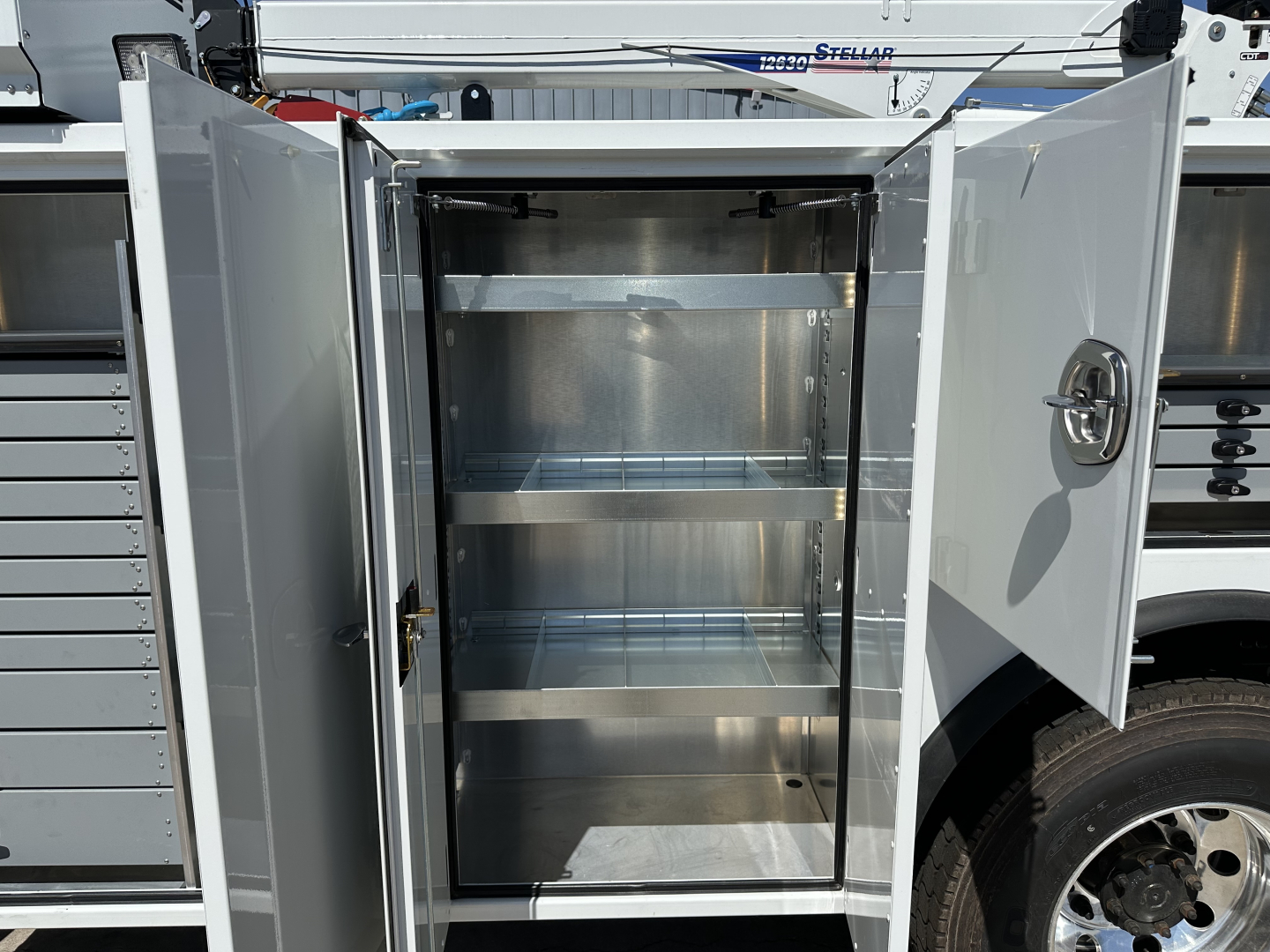 Service/Utility truck cargo cabinet with dual doors open, empty stainless steel shelves, securing latch visible on right door.
