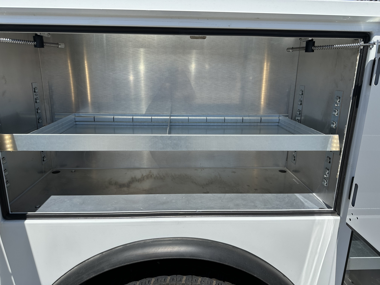 Service/utility truck cargo area with empty rack and metal storage compartments in a Mercedes-like utility bed. Appears to be a new 2026 Mack MD7 listing.