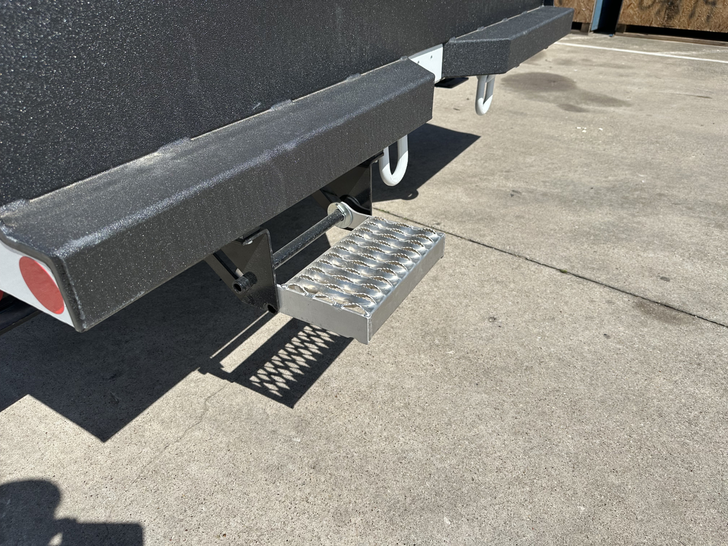 Step-up steel plate attached to rear of a new Mack MD7 truck chassis showing a perforated aluminum tread plate step and under-ride protection.