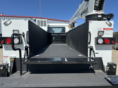Truck bed or service body area of a 2026 Mack MD7, flatbed with side panels raised, showing empty cargo space and rear hydrualic mechanism.