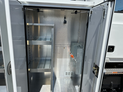 Service/utility truck cargo area with metal shelving and storage rack inside the cargo box of a 2026 Mack MD7 showing interior walls and hanging hooks.
