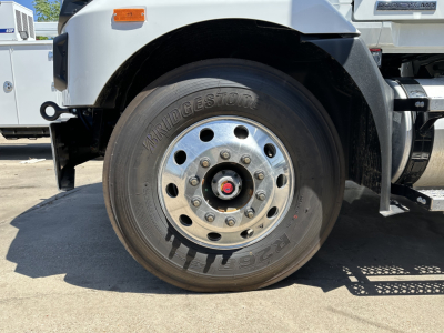 Front wheel of a new Mack MD7 service truck showing Bridgestone tire and chrome wheel with red center cap.