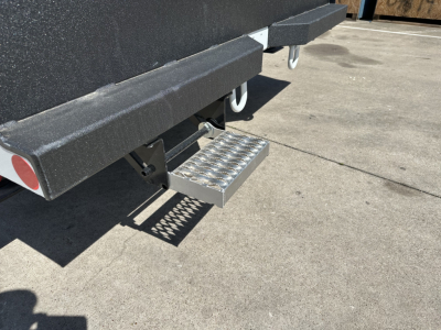 Step-up steel plate attached to rear of a new Mack MD7 truck chassis showing a perforated aluminum tread plate step and under-ride protection.
