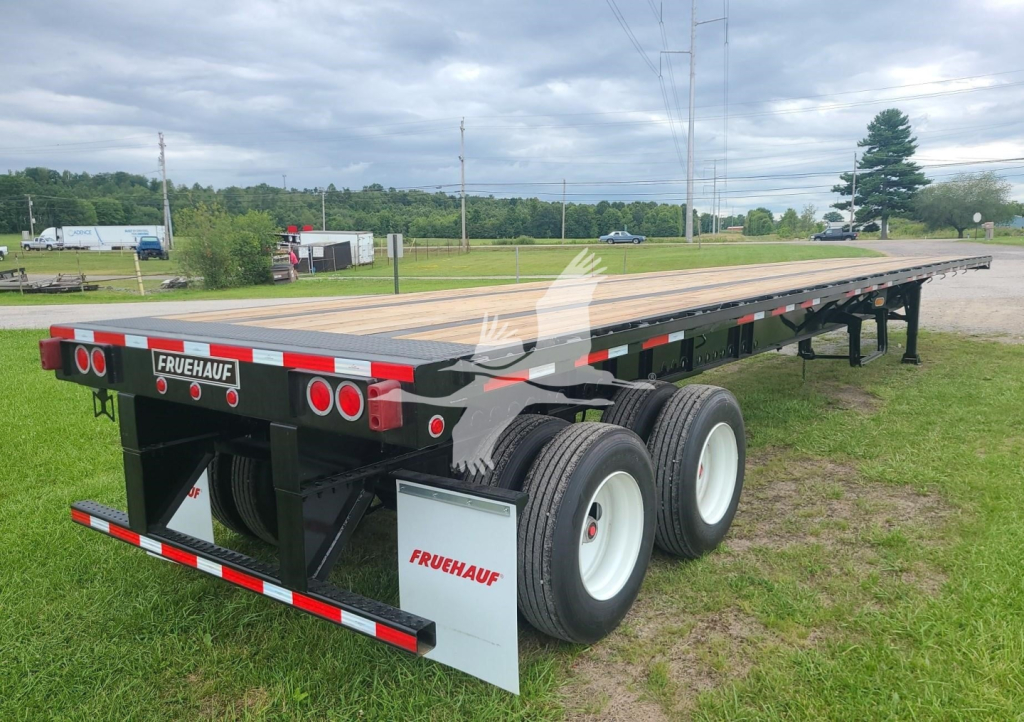 Fruehauf steel flatbed trailer showing rear and side with Fruehauf branding on mud flaps and triple-axle setup.
