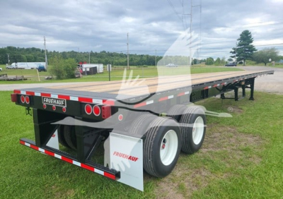 Flatbed trailer showing rear and side, Fruehauf branding, dual rear axle with white wheels, reflective safety stripes, mud flaps, and long steel deck.
