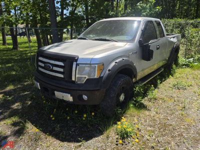Ford F-150 pickup truck extended cab 4x4 in a grassy lot with dandelions; silver body with black front grille and fender flares; badge on door; tires with clear tread.