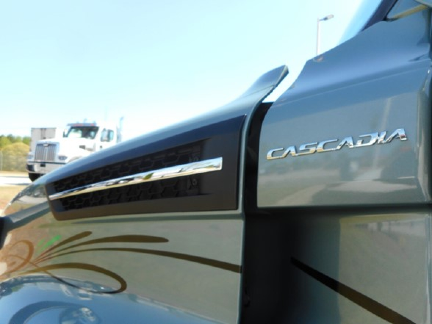 Truck side showing Freightliner Cascadia badge on the cab door inside a vehicle lot.