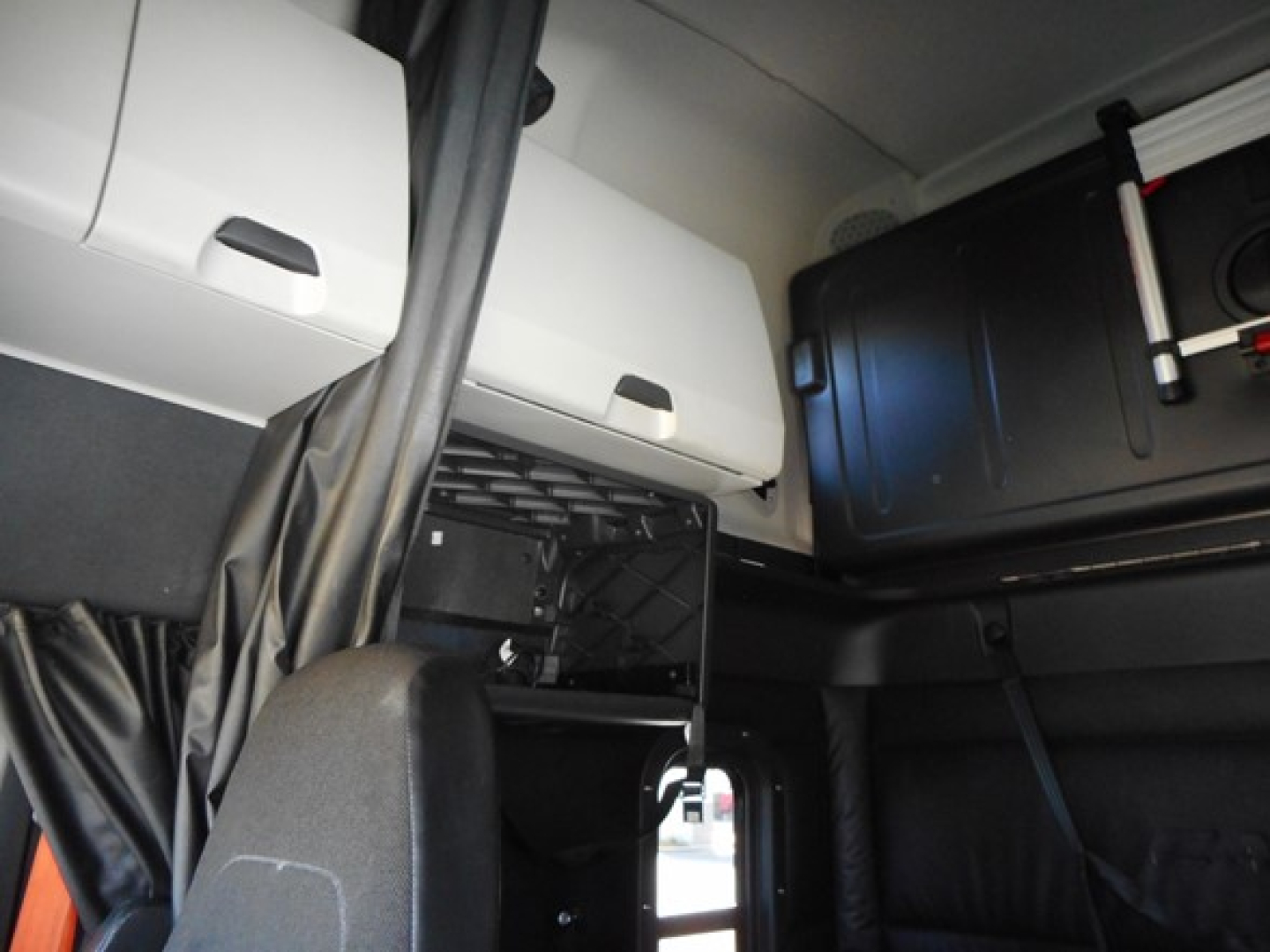 Truck engine bay area showing storage cabinets and a blue large plastic tank in the cab of a 2023 Freightliner Cascadia 126 sleeper cab.