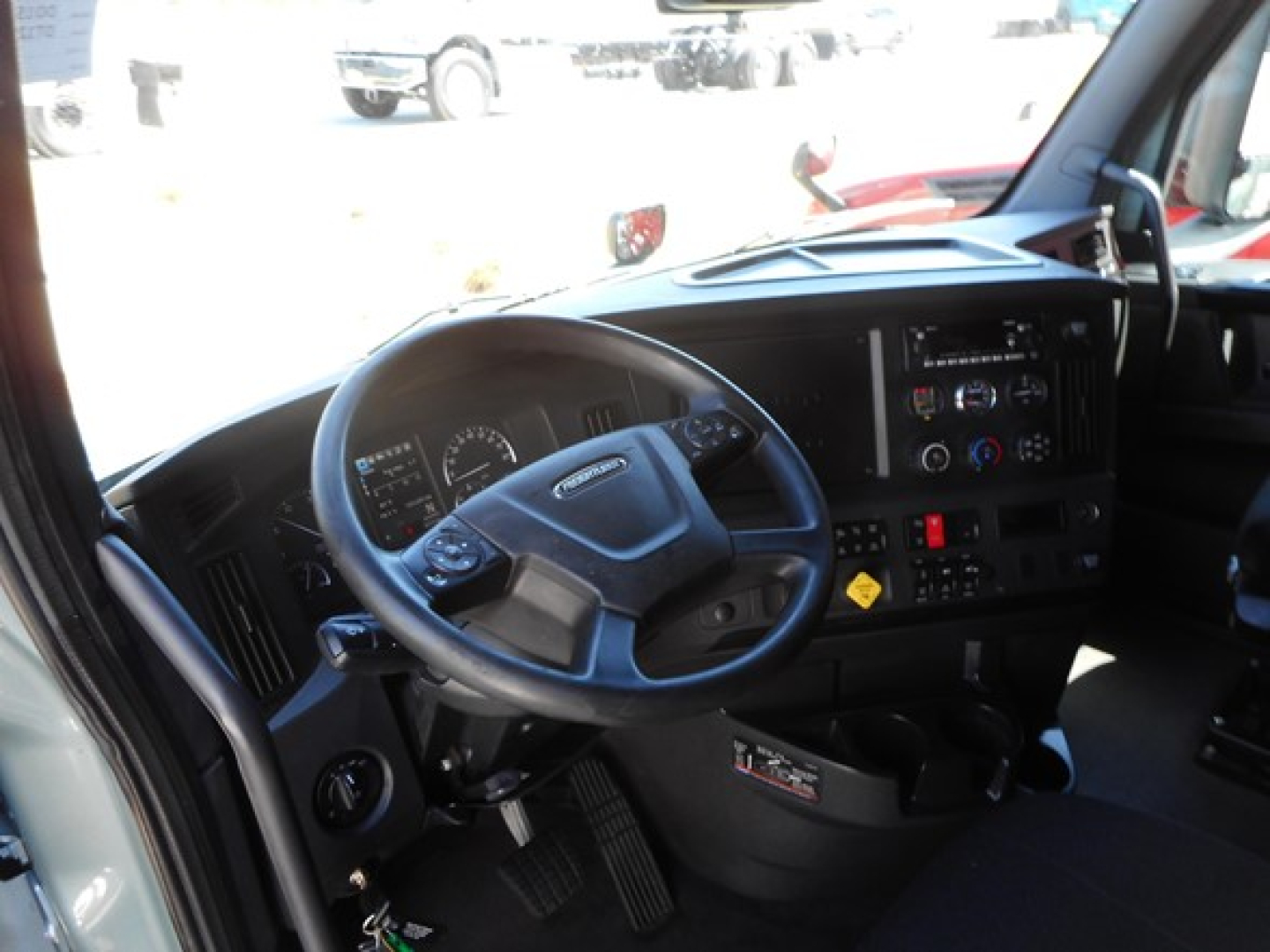 Truck cab interior showing steering wheel and dashboard of a Freightliner Cascadia, with gauges, control panel, and center console.