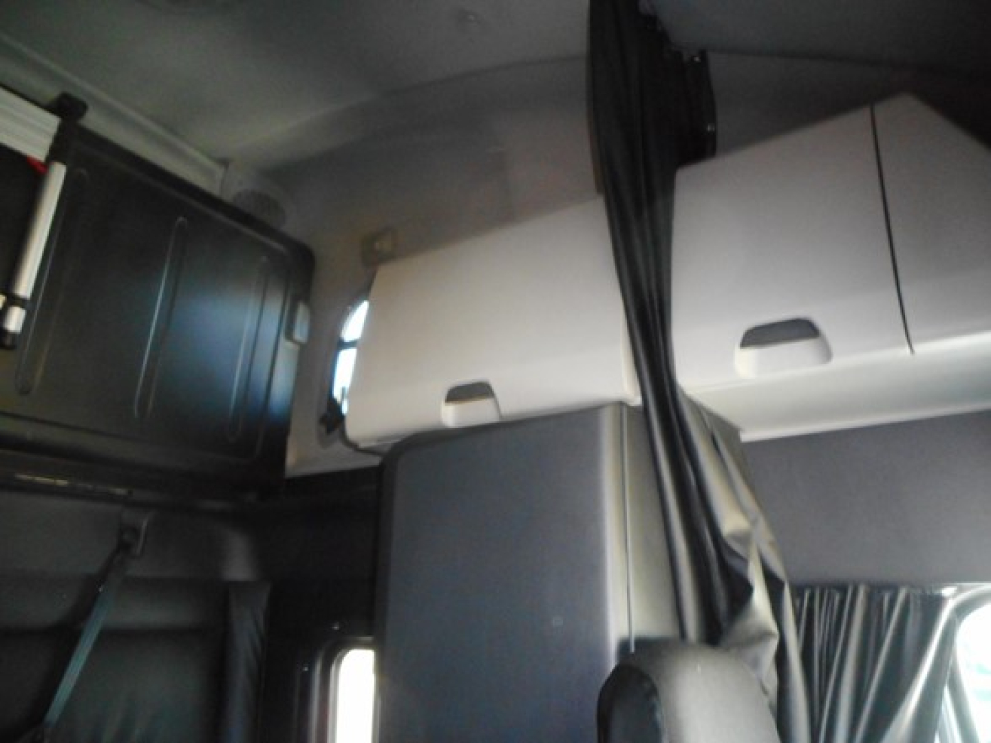 Interior cab area of a Freightliner Cascadia showing storage compartments and curtain, with seating and panels visible.