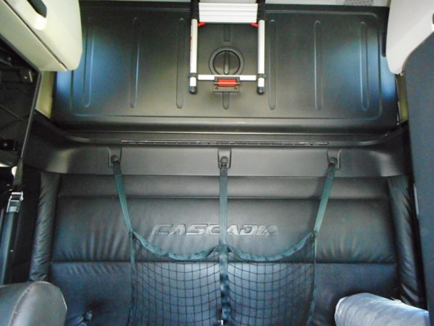 Freightliner Cascadia sleeper cab interior cargo area with strap nets and embossed Cascadia logo on seat/back panel.