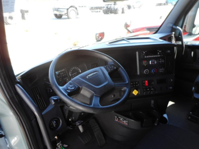 Truck cab interior showing steering wheel and dashboard of a Freightliner Cascadia, with gauges, control panel, and center console.