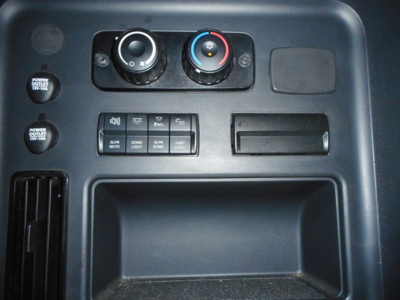 Dashboard controls and storage compartment area in a Freightliner Cascadia cab showing climate control dials, switches, and cup-holder/storage pocket.