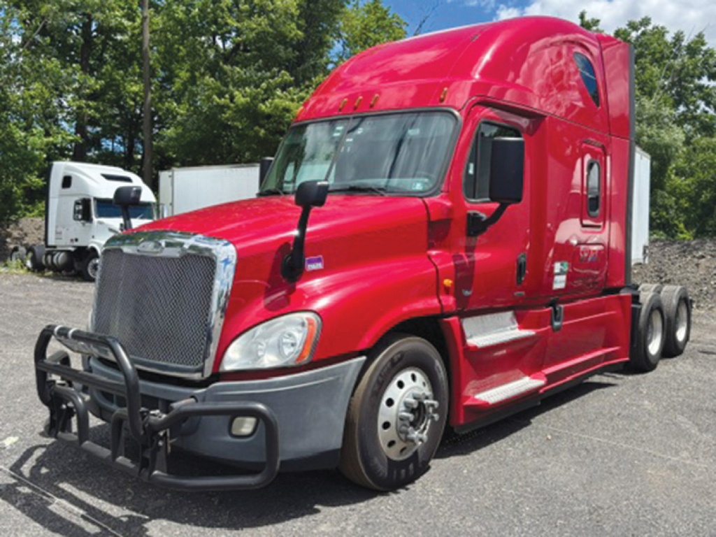Red Freightliner Cascadia125 truck in a lot, front grille guard visible, black side mirrors, dual rear wheels.