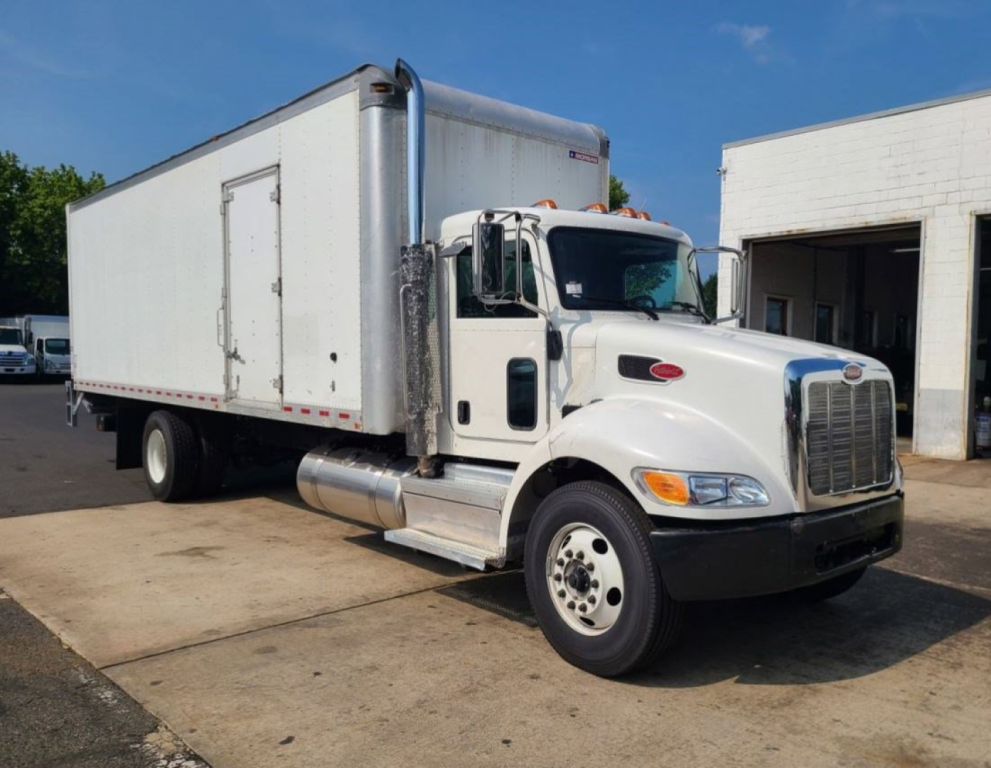 Peterbilt conventional box truck showing front and side view, white cab, large chrome grille, box cargo area, fuel tanks, and dual rear wheels.