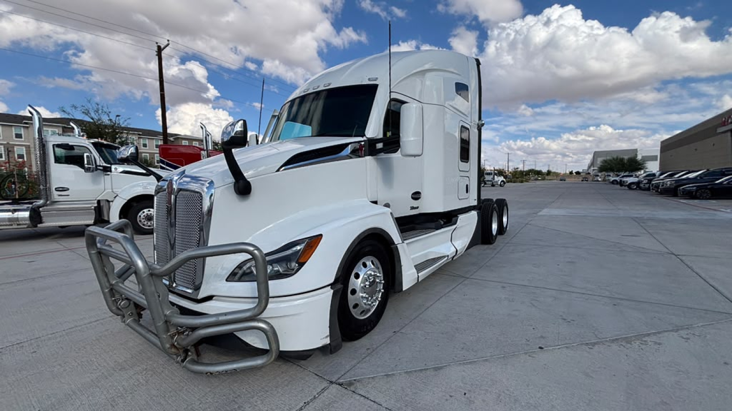 Kenworth T680 conventional sleeper tractor in white, front bull bar, side view, highway parking lot.