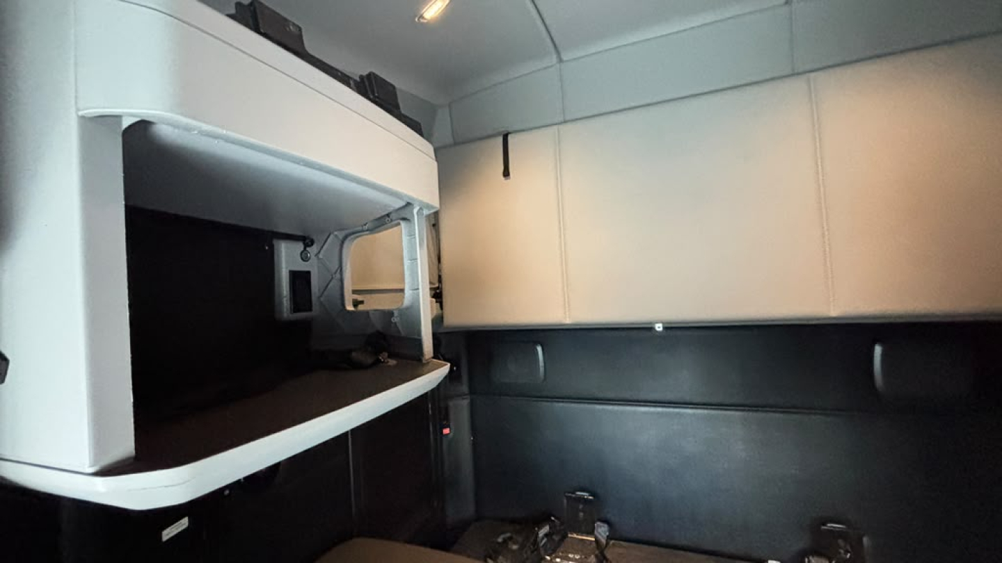 Kenworth T680 sleeper cab interior showing engine bay access area with a storage compartment and cab walls.