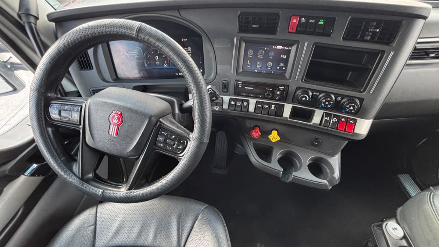 Kenworth T680 dashboard and steering wheel interior showing steering wheel with logo, touchscreen display, control knobs, and gear shifter.