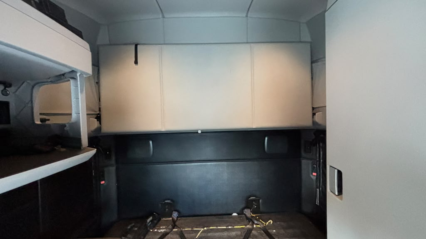 Kenworth T680 interior sleeper cab cargo area showing side cabinets and overhead storage, vertical jump seats or bunk area, and light gray panels
