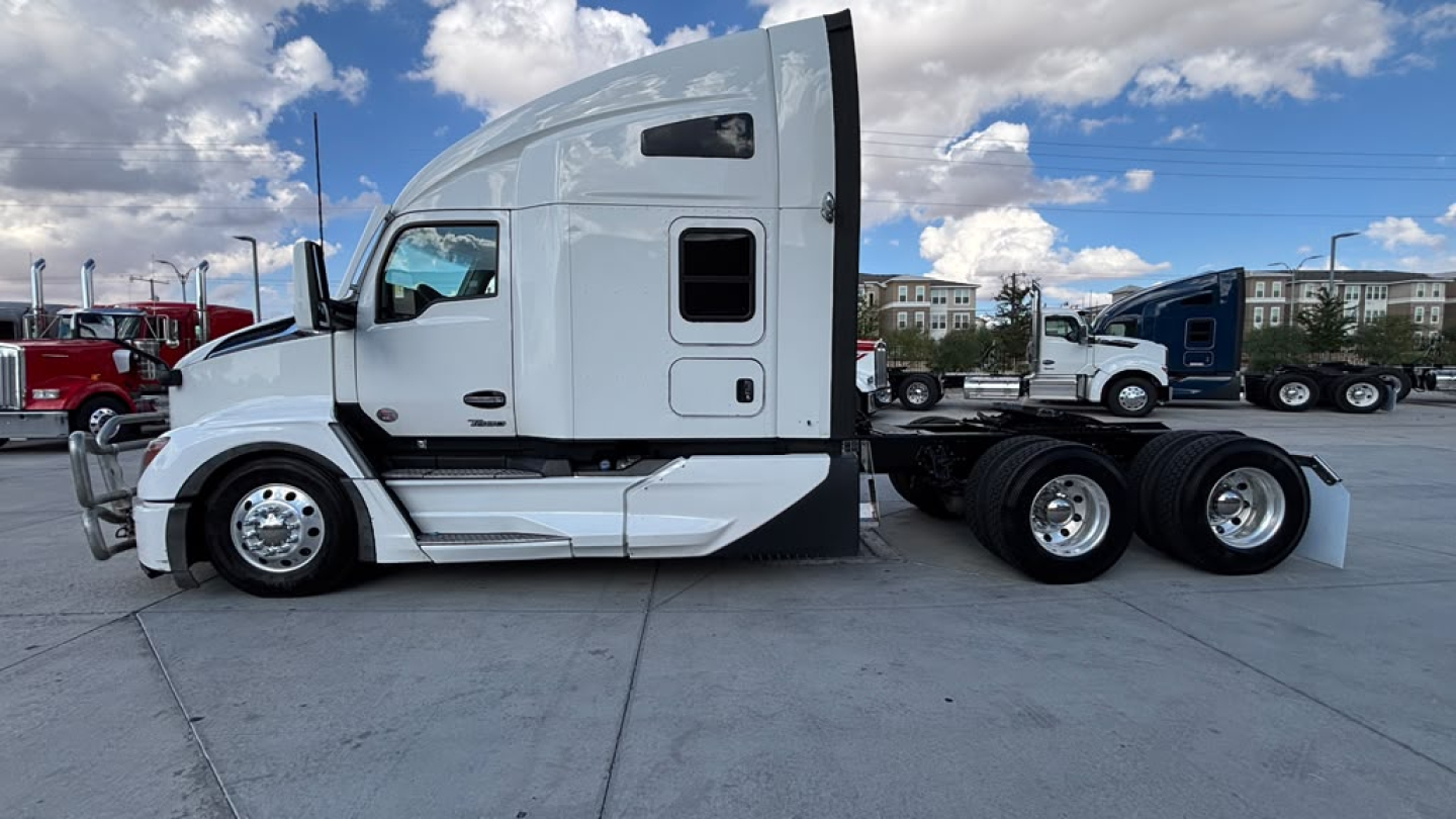 Kenworth T680 tractor side view showing sleeper cab with white paint and dual rear axles. Visible text not legible; features include windows, door, and fuel tanks.