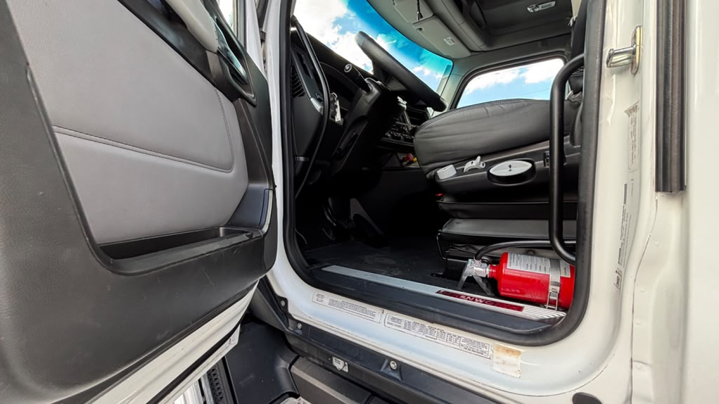 Kenworth T680 truck cab interior showing entry area and driver's seat with steering wheel, dashboard, and floor area; door open.
