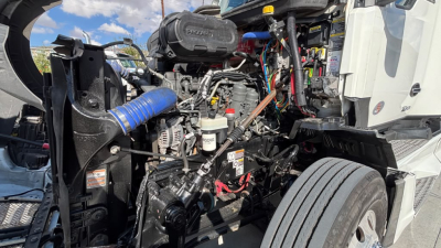 Kenworth T680 engine bay showing diesel engine components, hoses, wiring, and air intake with surrounding cab frame.