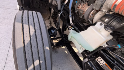 Kenworth T680 engine bay showing coolant reservoir and various hoses and components.