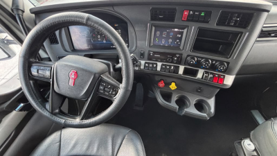 Kenworth T680 dashboard and steering wheel interior showing steering wheel with logo, touchscreen display, control knobs, and gear shifter.