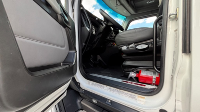 Kenworth T680 truck cab interior showing entry area and driver's seat with steering wheel, dashboard, and floor area; door open.