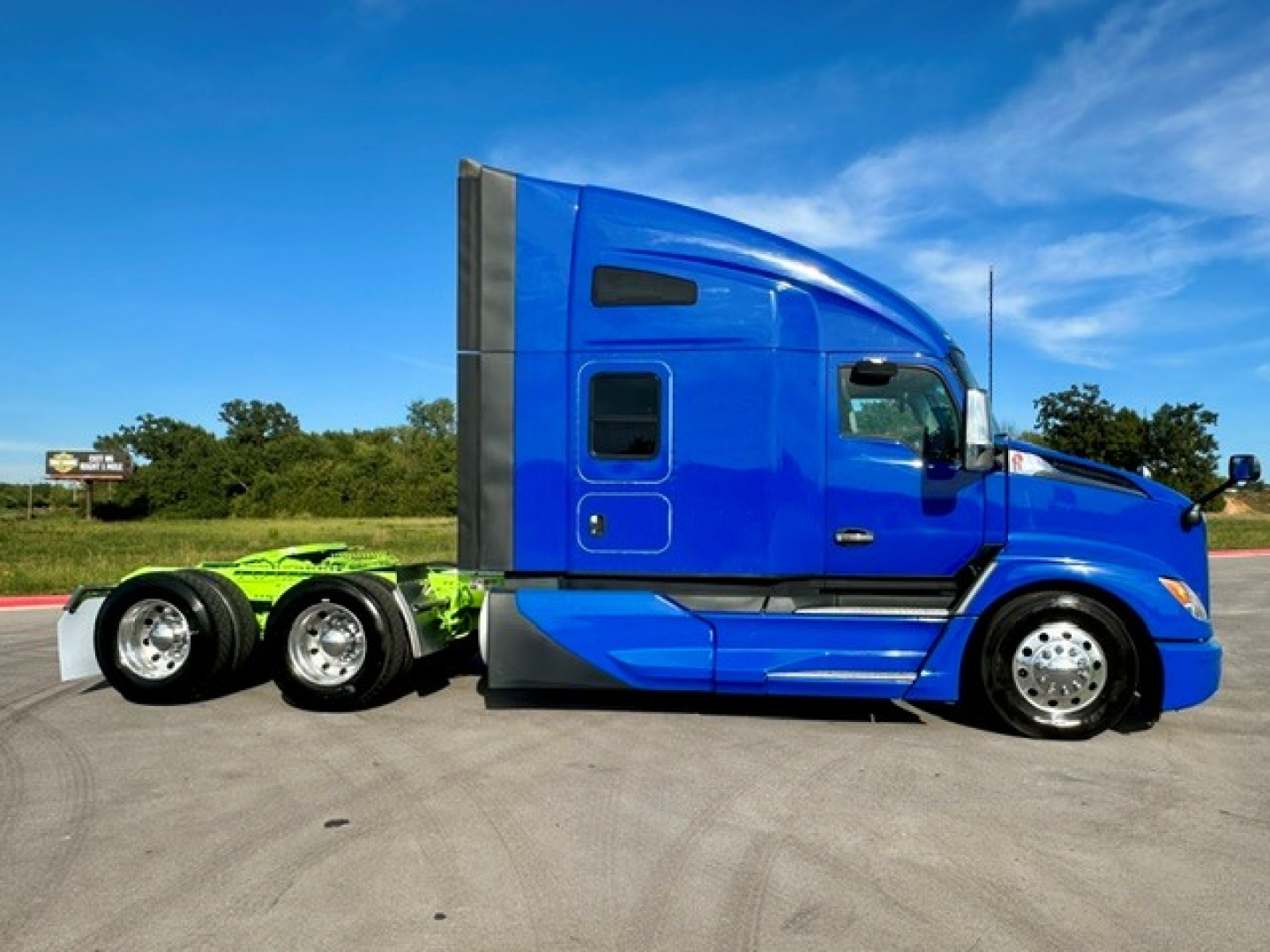 Kenworth T680 tractor-trailer side view showing blue cab and green chassis with chrome wheels.