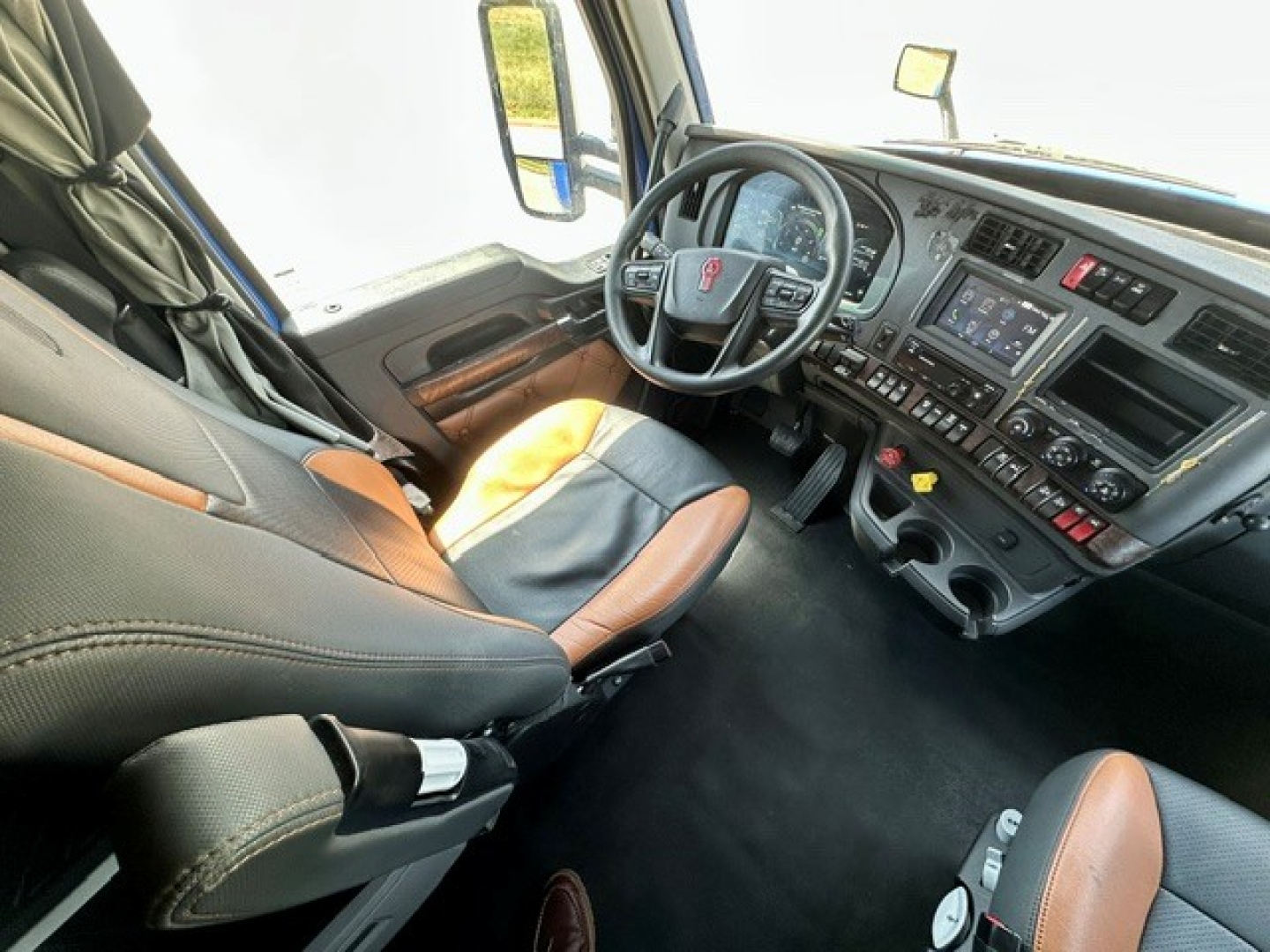 Kenworth T680 cab interior showing steering wheel, dashboard, and driver seat with black and tan upholstery.
